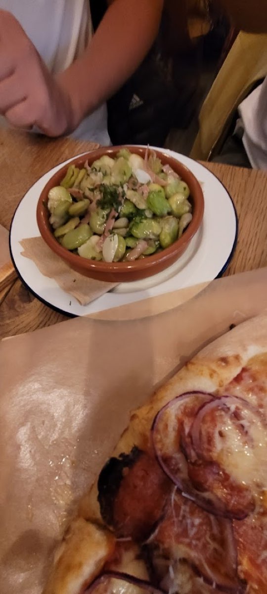 Sałatka z bobu z ziołami i czerwoną cebulą w glinianej miseczce, obok kawałek pizzy.