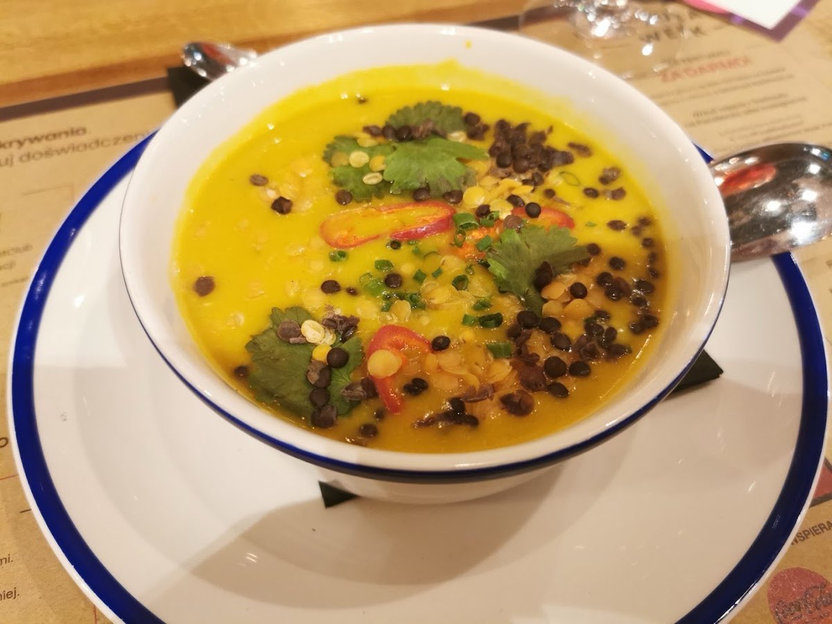 Aromatyczna żółta zupa z soczewicą, kolendrą i chili w głębokiej misce z niebieskim rantem.